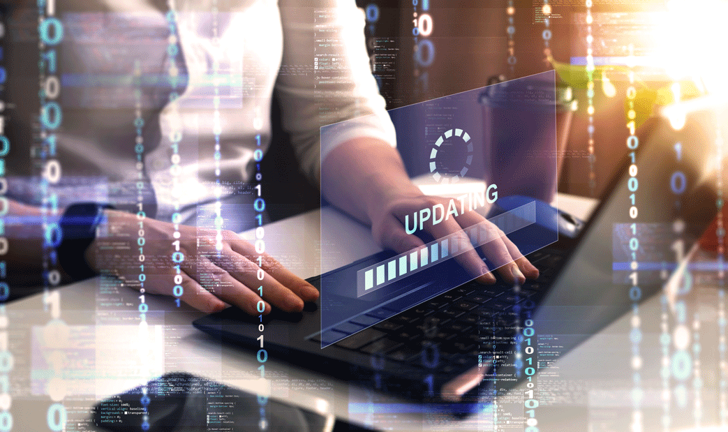 Person typing on a laptop with a digital overlay showing the word ‘UPDATING,’ a progress bar, a circular loading icon, and background layers of binary digits and programming code.